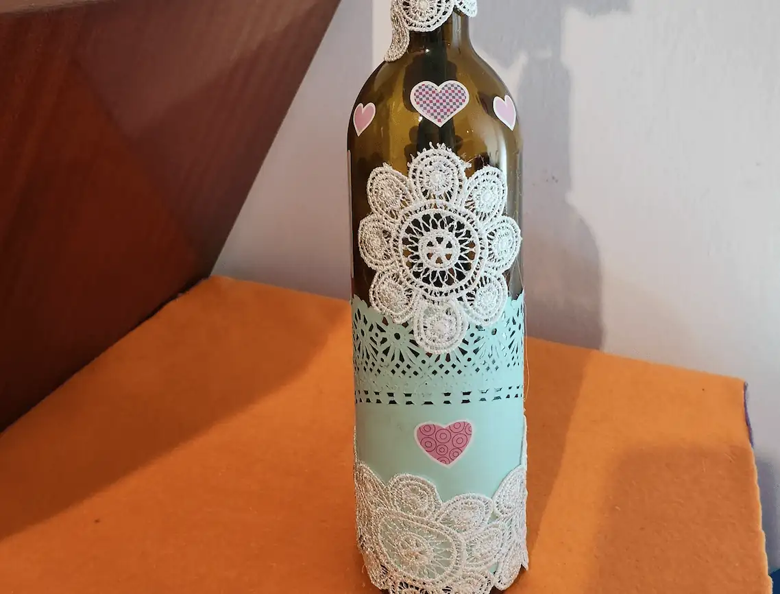 Botella de cristal con encajes y dos flores